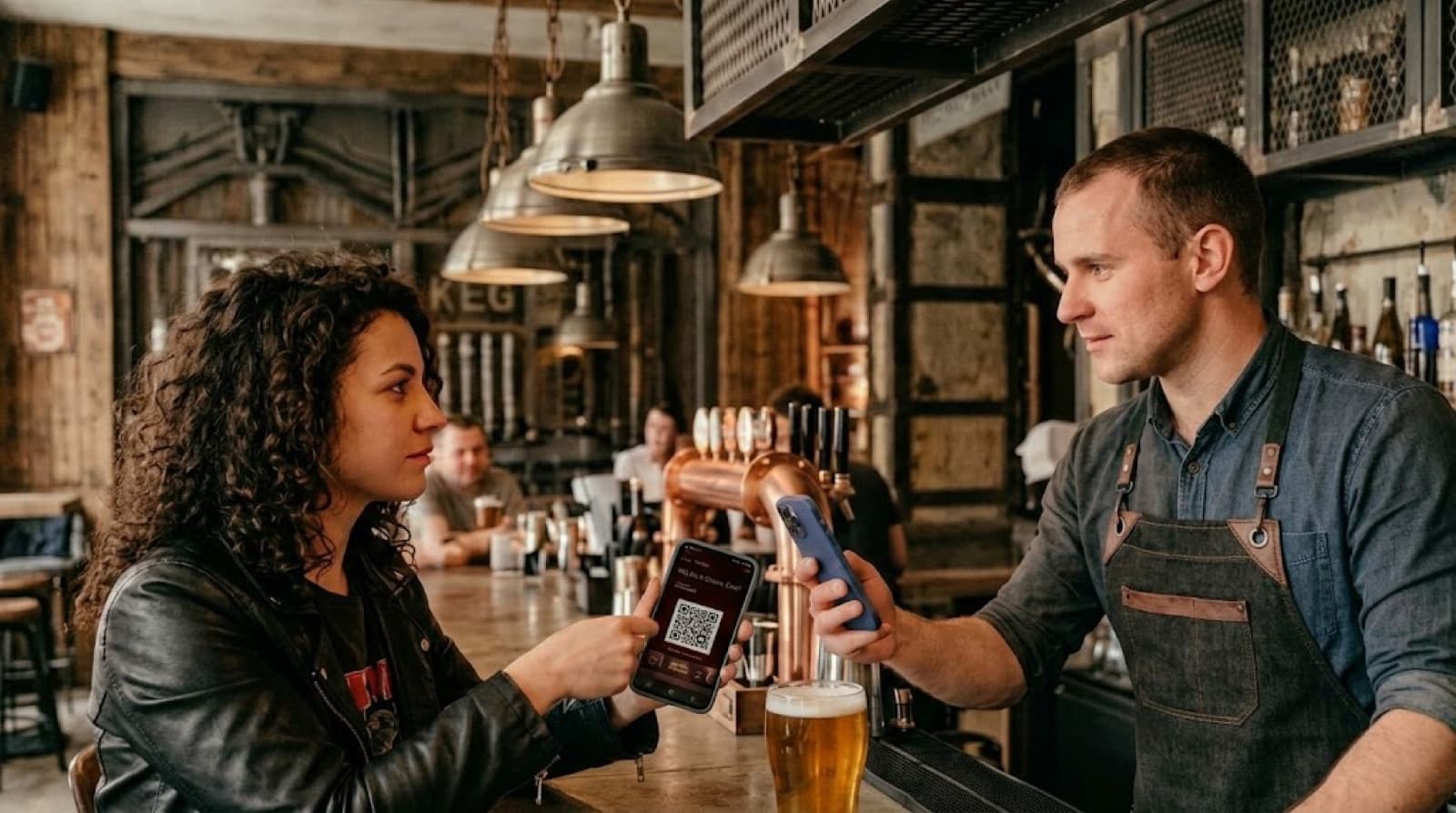 Klientka przy barze w pubie pokazuje kartę lojalnościową na telefonie, a barman ją skanuje